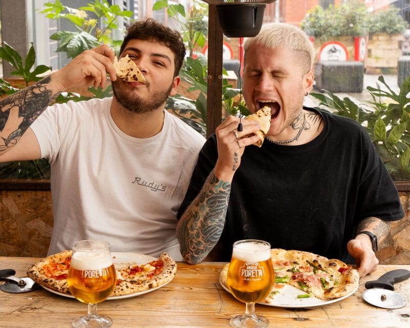 two men biting into neapolitan pizza slices